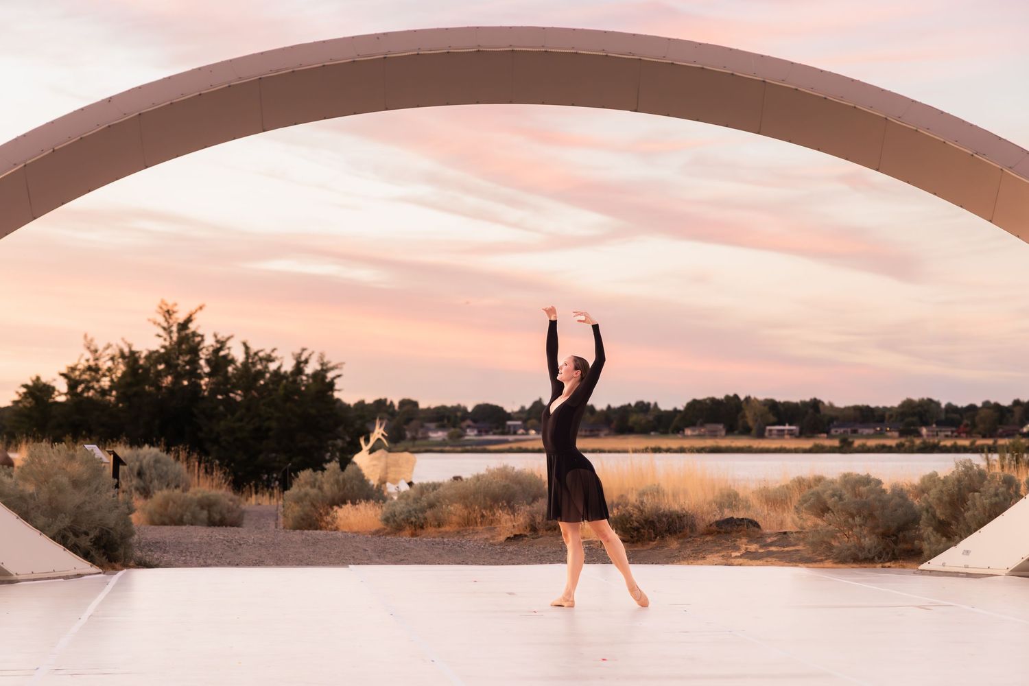 A silhouette dances under a curved architectural arch at sunset with desert landscape in the background.