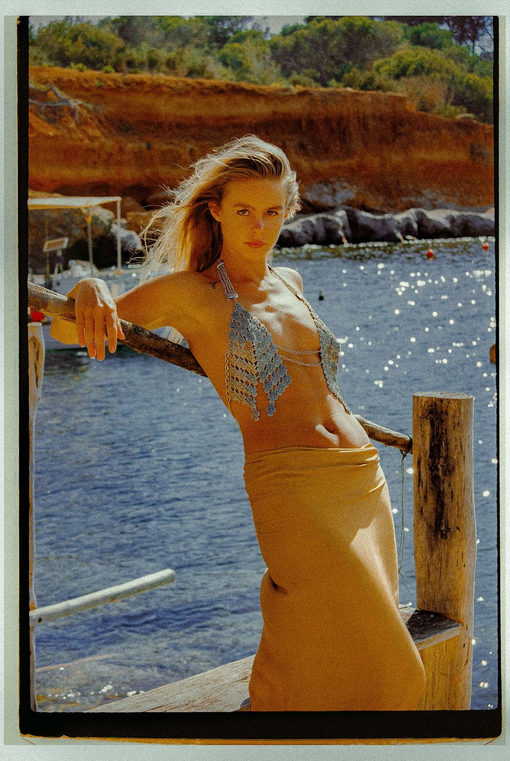 Woman in a patterned bikini poses near sparkling water on a sunny beach dock.