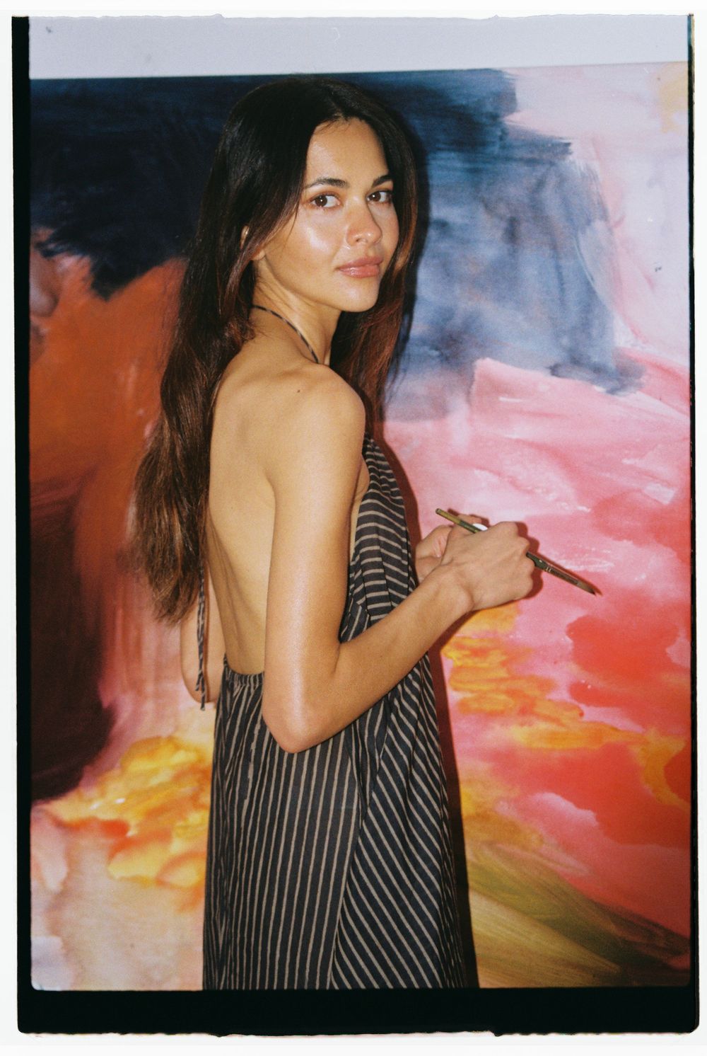A person in a striped dress poses against a vibrant sunset-colored backdrop in a series of artistic polaroid-style photos.