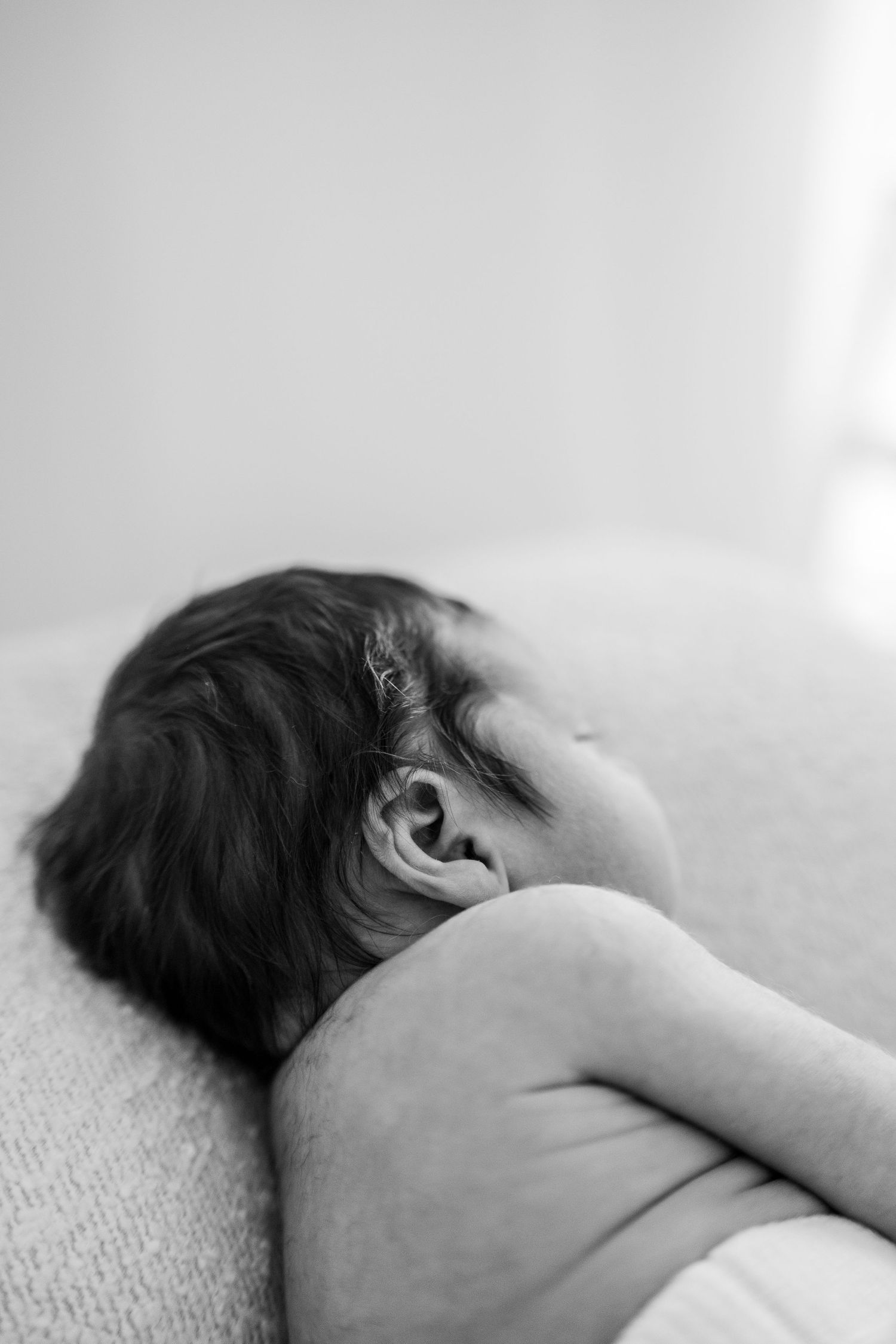 A black and white artistic photograph shows a sleeping figure resting on textured fabric.