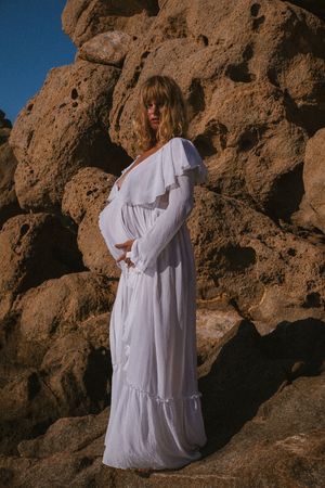 Figure in flowing white dress poses against rocky desert formations at sunset.