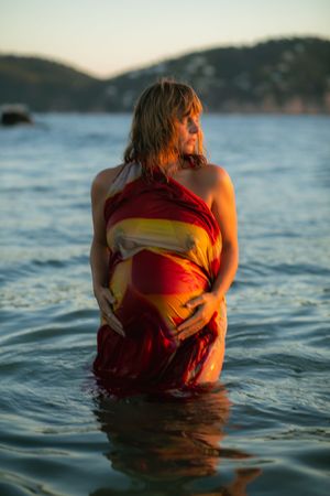 Two figures embrace while partially submerged in calm ocean waters during golden hour.