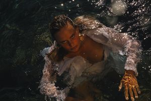 Artistic underwater portrait with sparkling bubbles and floating fabric in dark water.