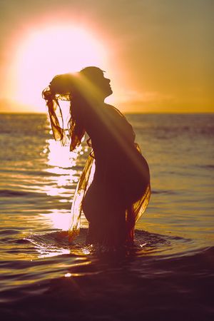Dramatic silhouette of a person emerging from water against a golden sunset sky.