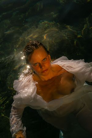 Ethereal underwater portrait with flowing white fabric and dramatic lighting against a dark background.