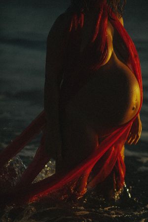 Artistic silhouette emerges from dark water illuminated by dramatic red lighting.