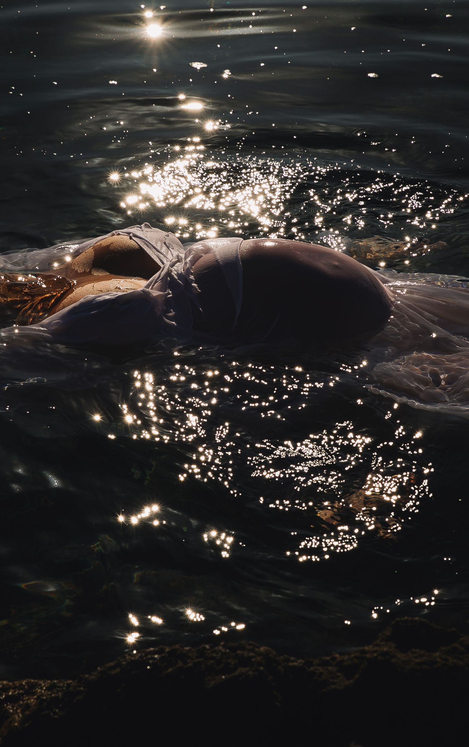 Ethereal reflections of sunlight dance across dark rippling water creating a mesmerizing pattern of sparkles.
