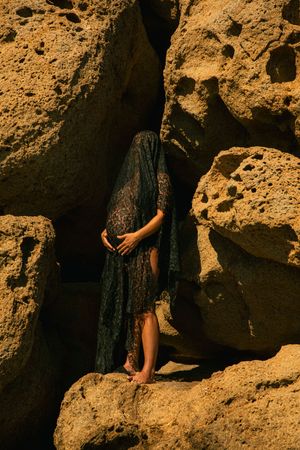 Figure in dark dress poses against textured golden cliff face in dramatic lighting.
