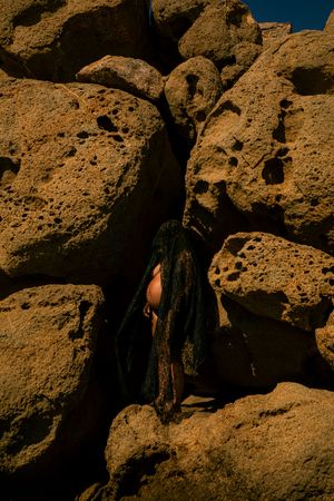Person in dark clothing blends with shadows among sun-lit coastal rock formations.