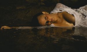A person lies submerged in dark water wearing white clothing creating a haunting artistic composition.