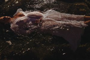 A figure in a flowing white dress floats ethereally in dark water creating a dreamy underwater scene.