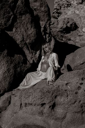 Monochrome image of figure in light clothing posed among dark rocky formations.