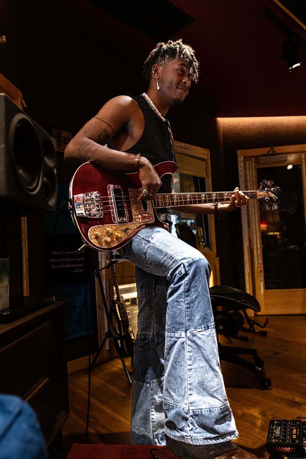 Musician playing electric guitar in recording studio wearing distressed jeans in dramatic lighting.