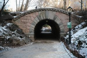 Stone bridge covered in snow spans across a frozen stream in Central Park during winter.