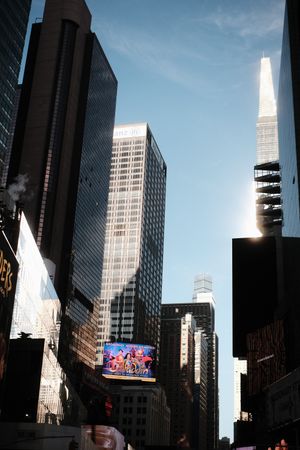 Modern skyscrapers and digital billboards rise against a bright blue sky in New York City.