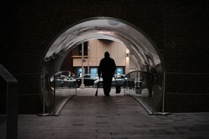 Dark tunnel walkway with arched ceiling and silhouetted figures in the distance.
