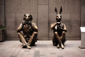 Bronze sculpture installation of seated figures along stone wall.