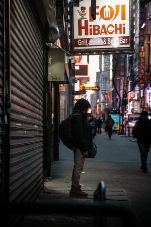 Dark urban street scene with illuminated storefront signs and metal security gates.