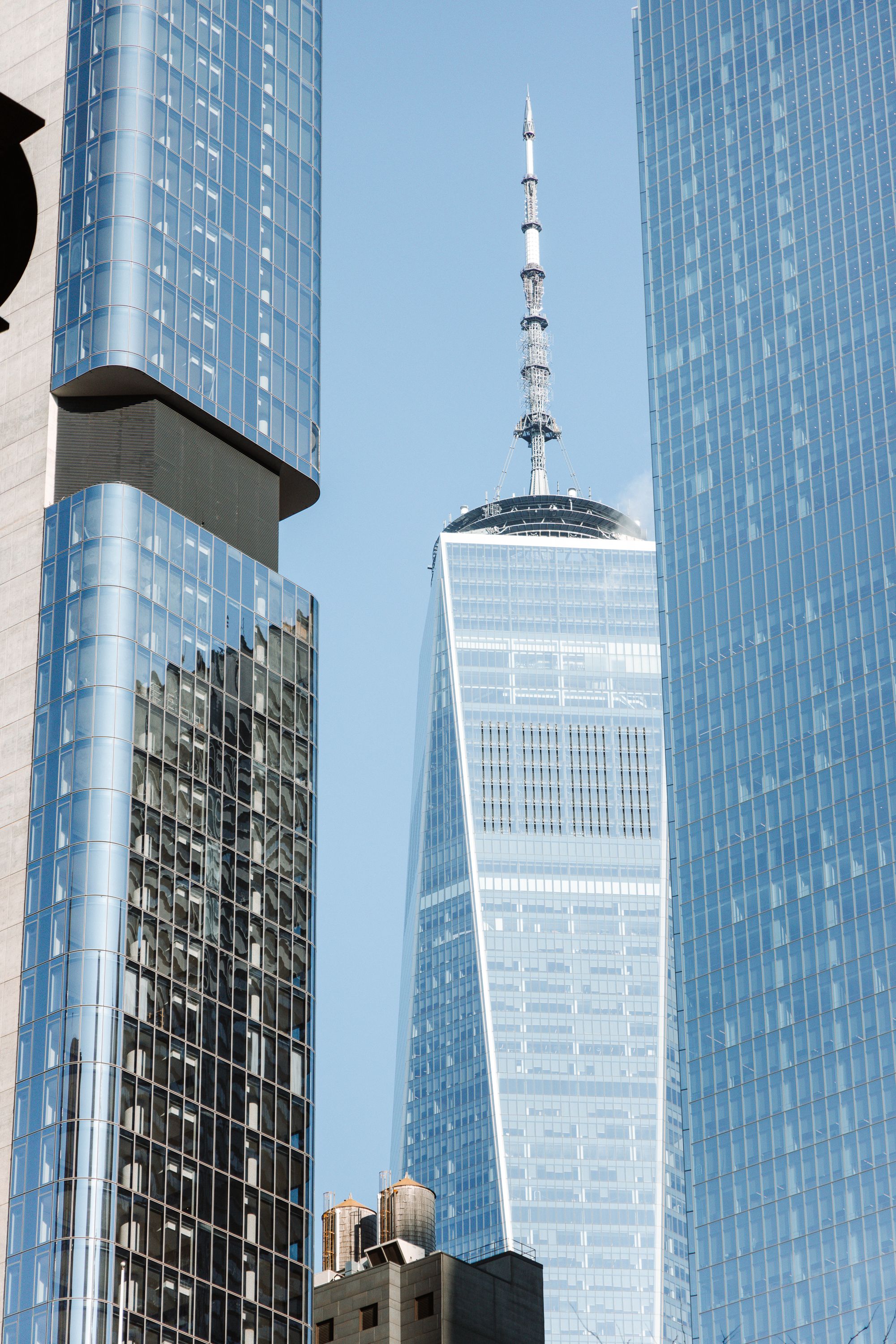 Modern glass skyscrapers and One World Trade Center tower against clear blue sky.