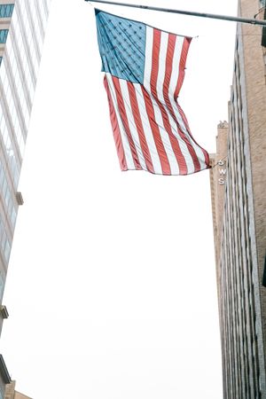 American flags waving against modern glass skyscrapers in an urban setting.