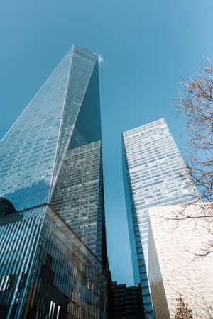 Modern glass skyscraper with angular architecture reflects bright blue sky.