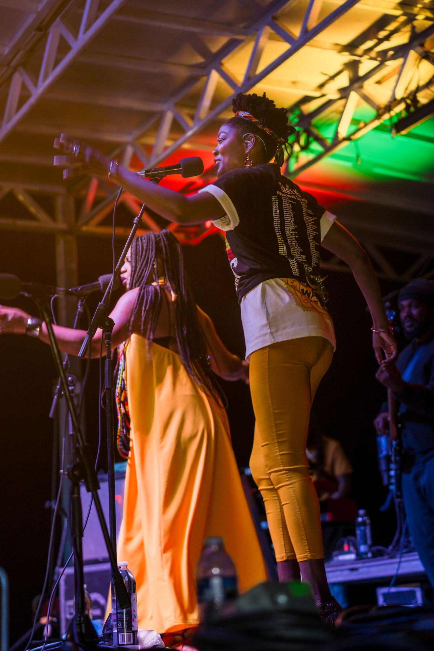 Musicians perform on stage under colorful lighting at a concert venue with vibrant orange and green illumination.