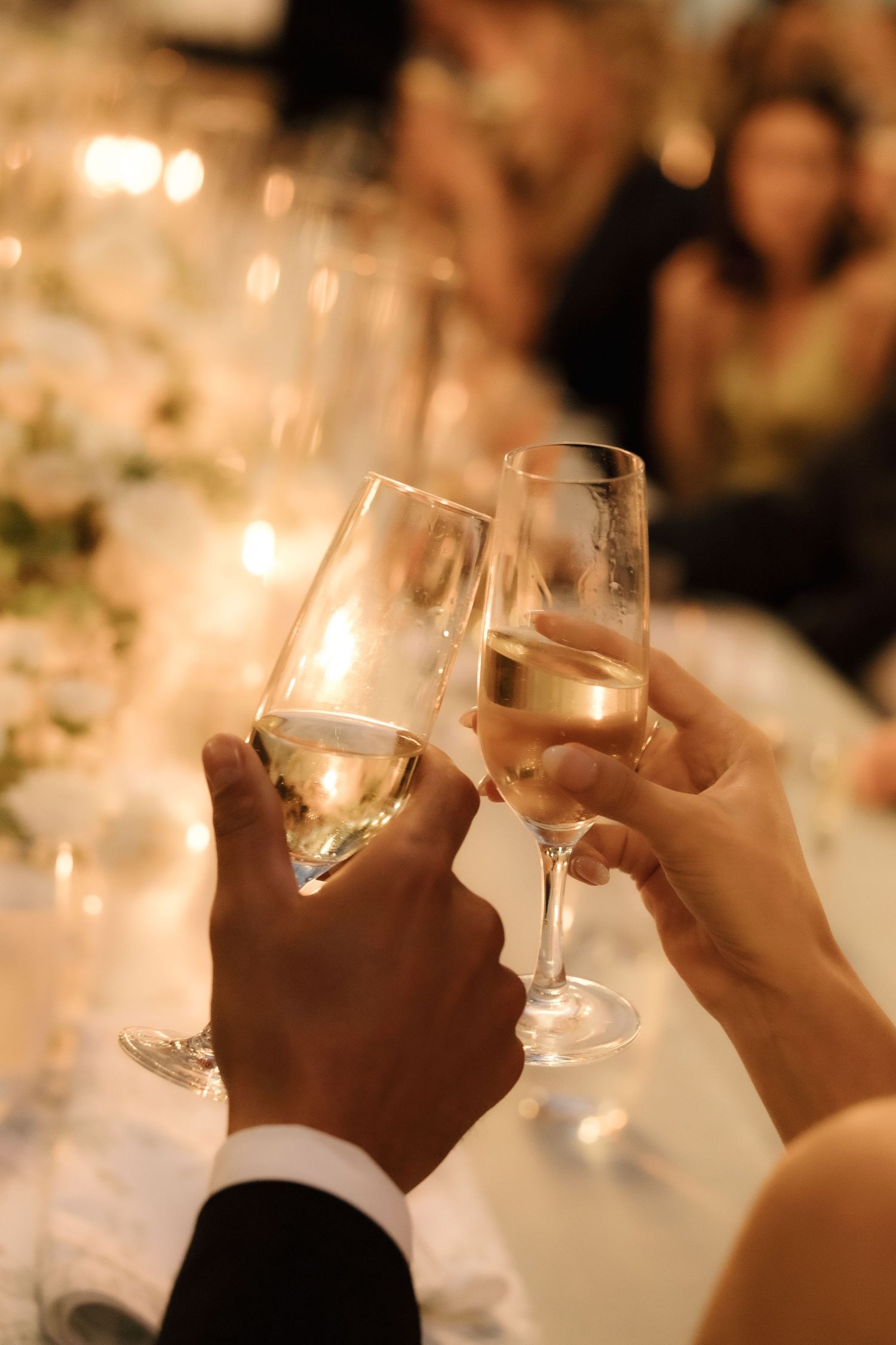 Hands holding wine glasses during a toast at an elegant candlelit dinner party.