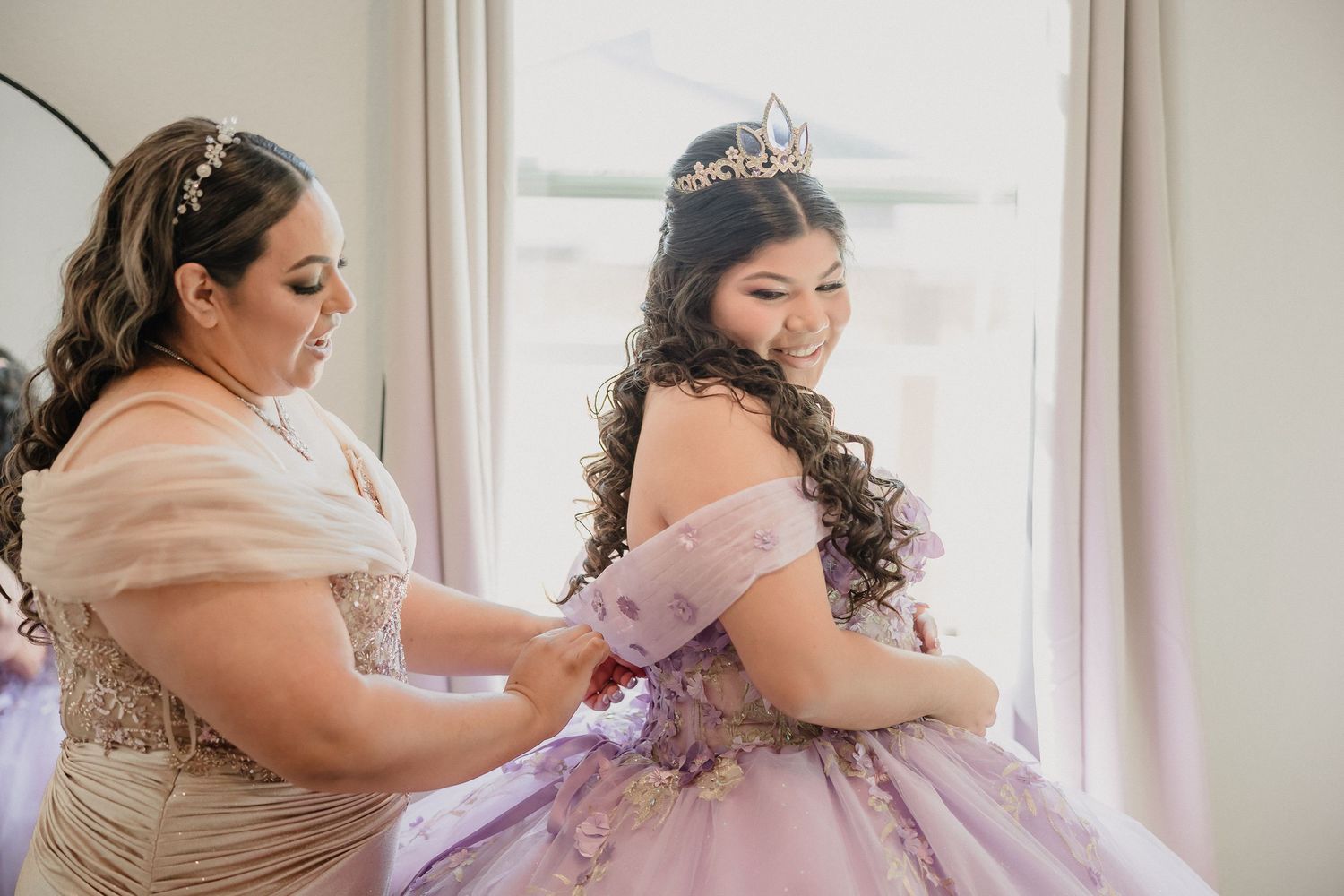 Quinceanera gets ready in a bright room with mom helping her prepare for the ceremony.
