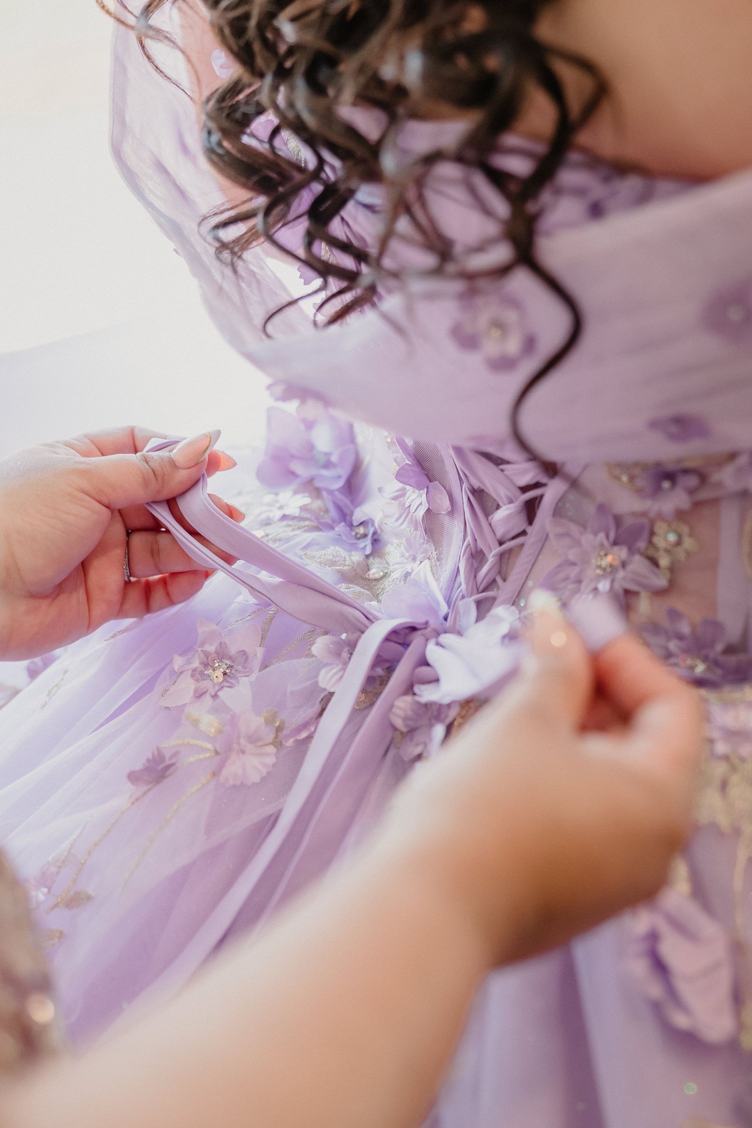 Close-up details of delicate purple and white lace embellishments being sewn onto a formal gown.