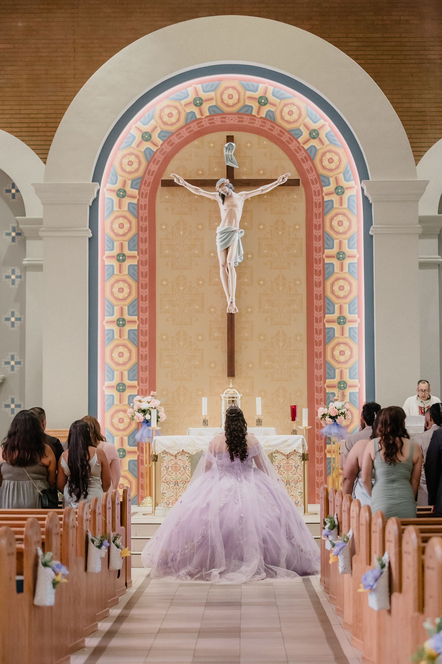 A quince in a lavender quinceañera dress in an ornate church during a religious ceremony.