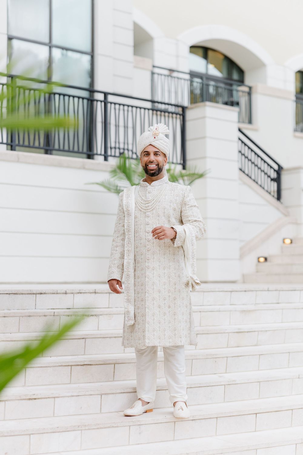 Person wearing white traditional Indian outfit poses on white stone steps with architectural details visible.