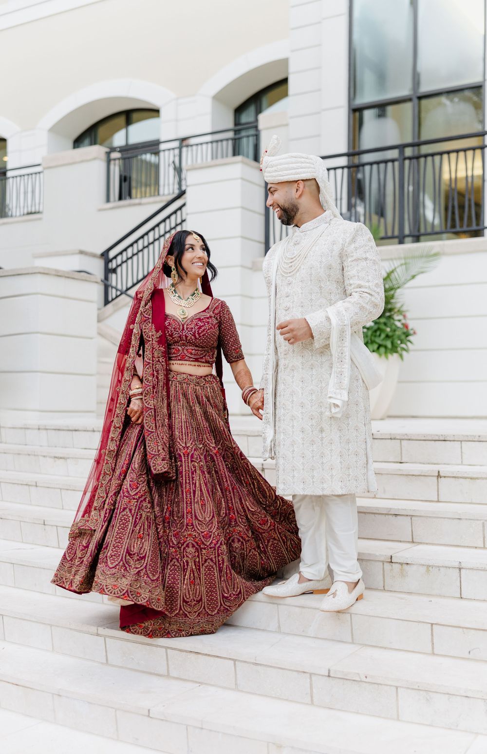 A couple in traditional South Asian wedding attire poses on white stone steps for romantic wedding photos.