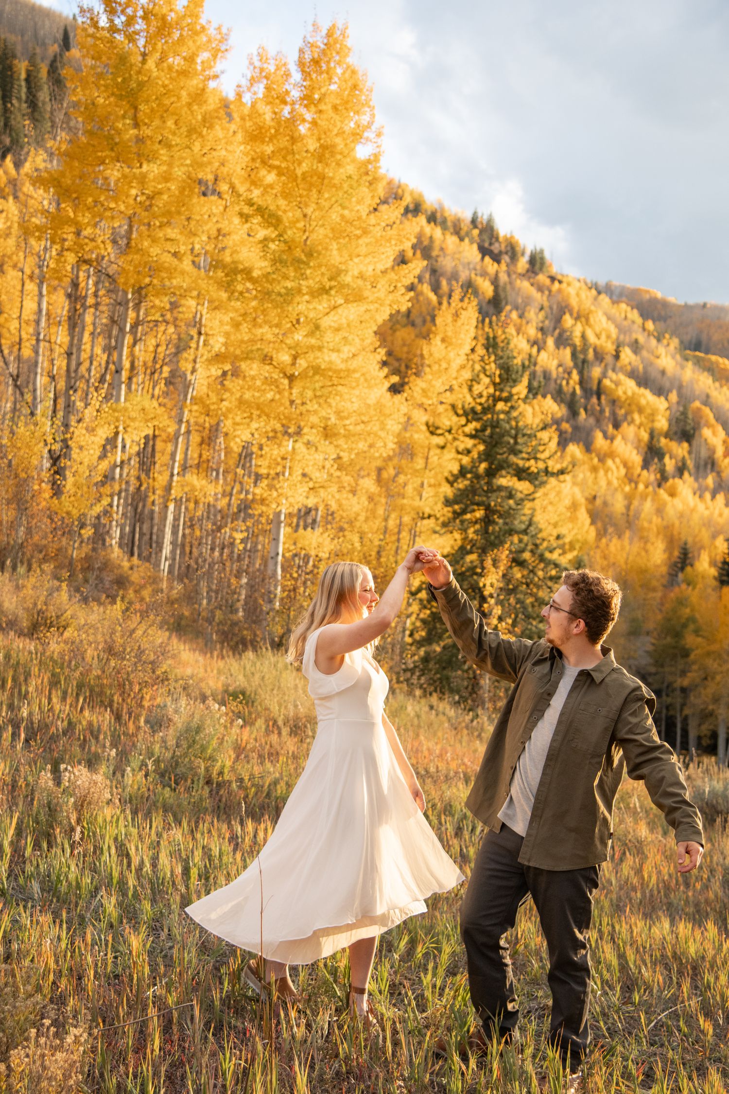 Vail fall engagement photo session with a dancing couple romantically frolicking in a field with golden aspen leaves and trees
