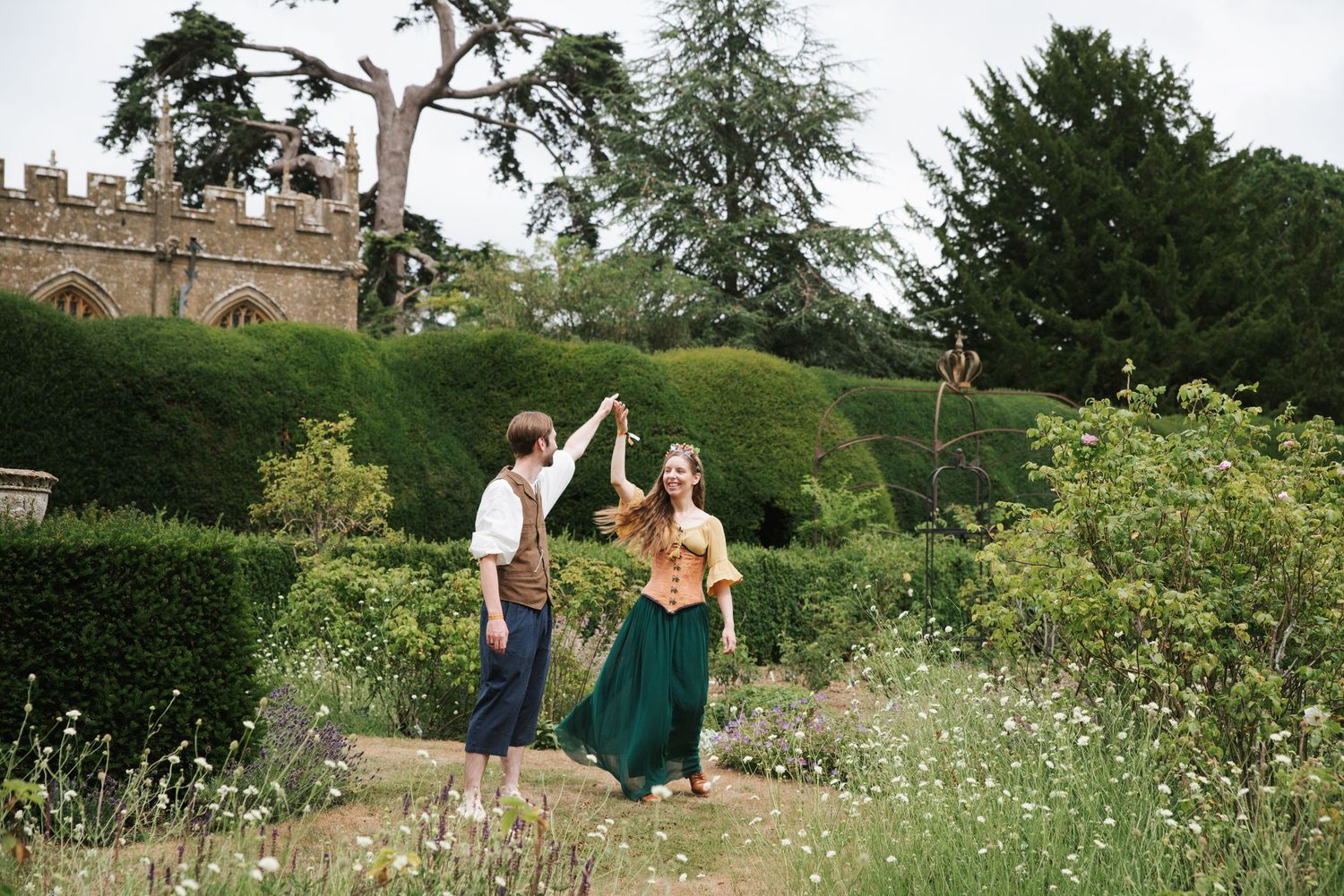 Two figures dancing joyfully in a garden with a castle wall visible in the background.