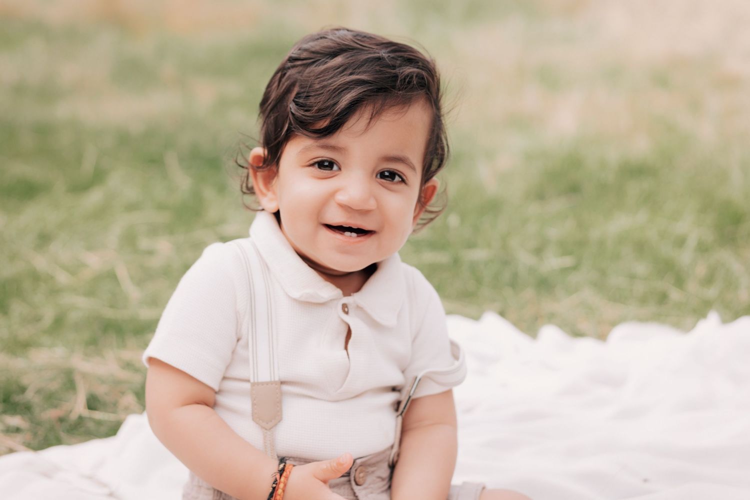 Child smiling while lying on white blanket during outdoor photo session.