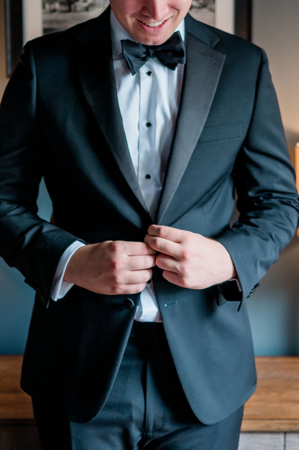 Close-up shots of a groom buttoning his classic black tuxedo jacket before the wedding ceremony.