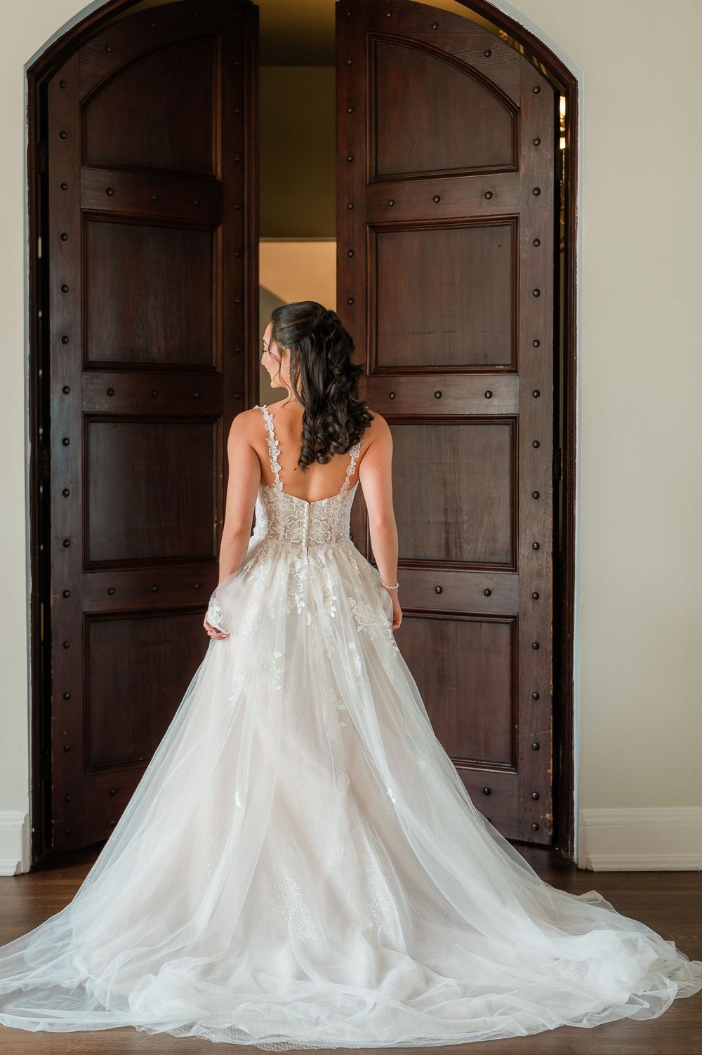 Back view of an elegant lace wedding gown with long train against wooden doors.