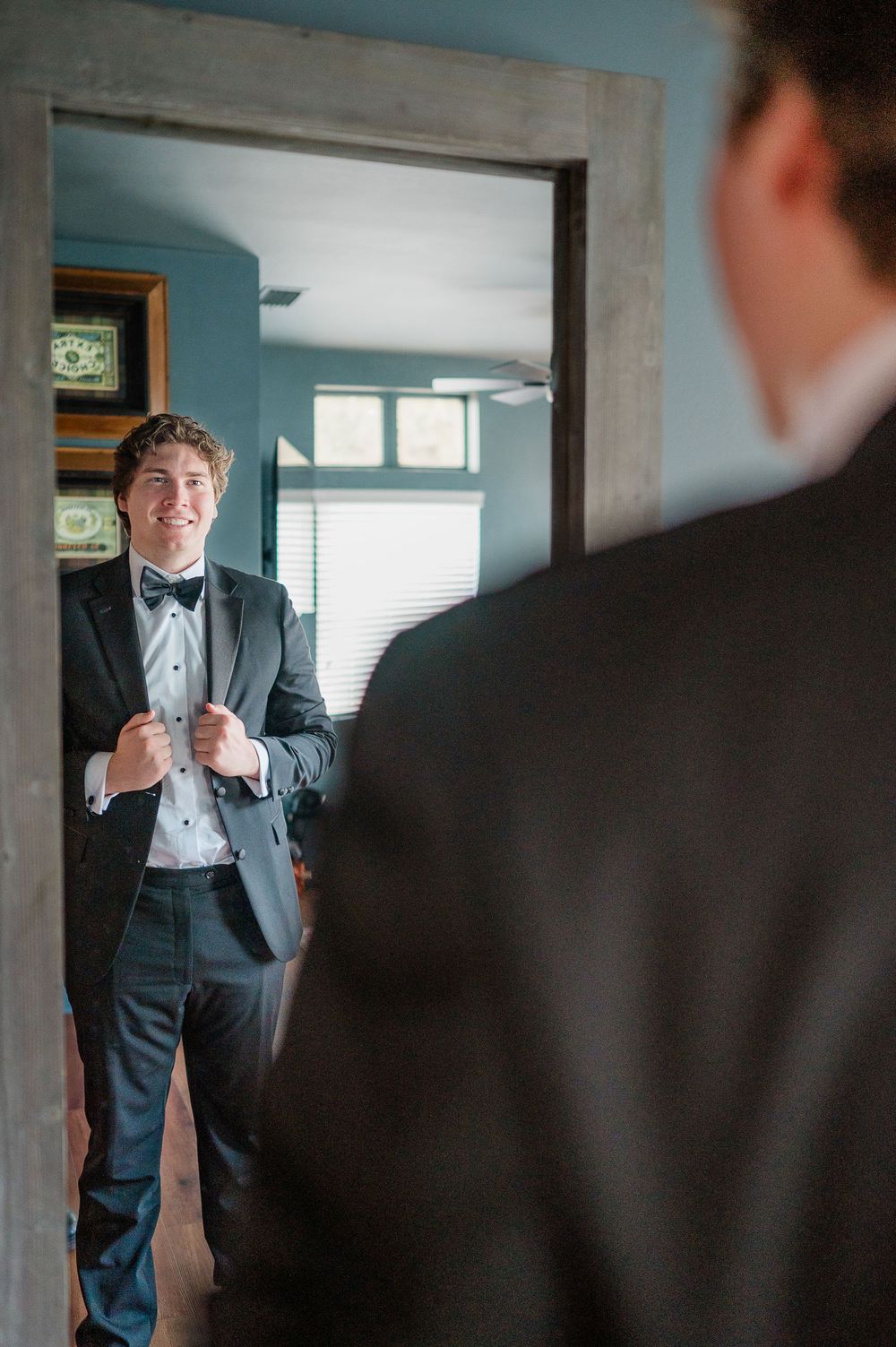 Wedding party members in formal attire adjusting bowties and getting ready in a blue-walled room.