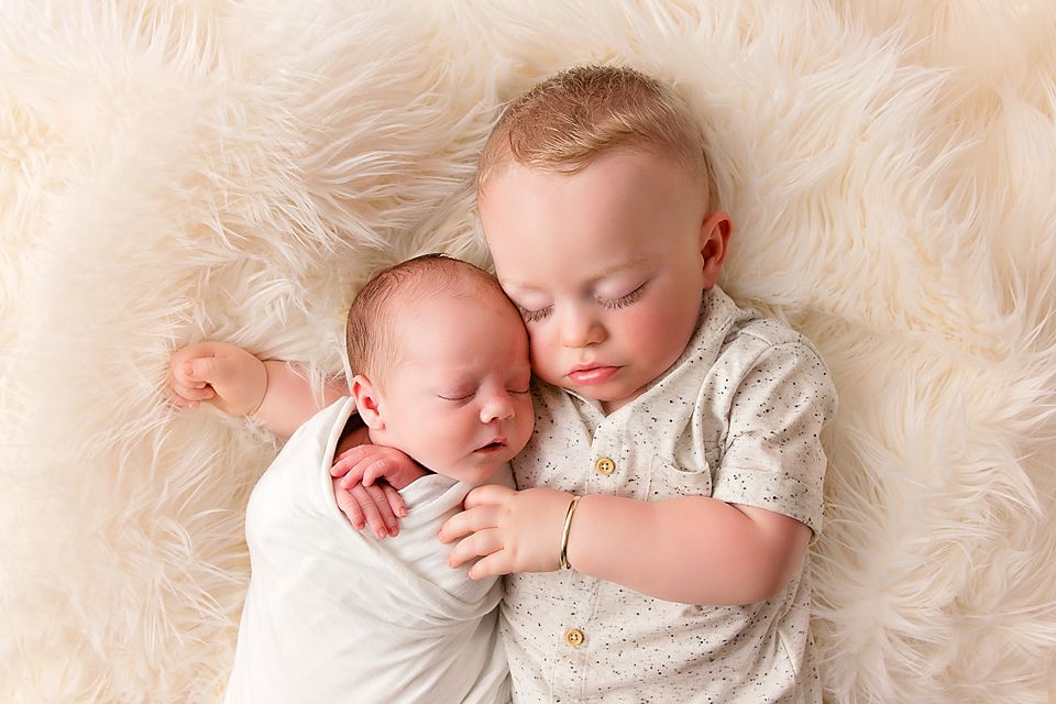 Sleeping baby in white clothing resting on plush cream-colored fur blanket.