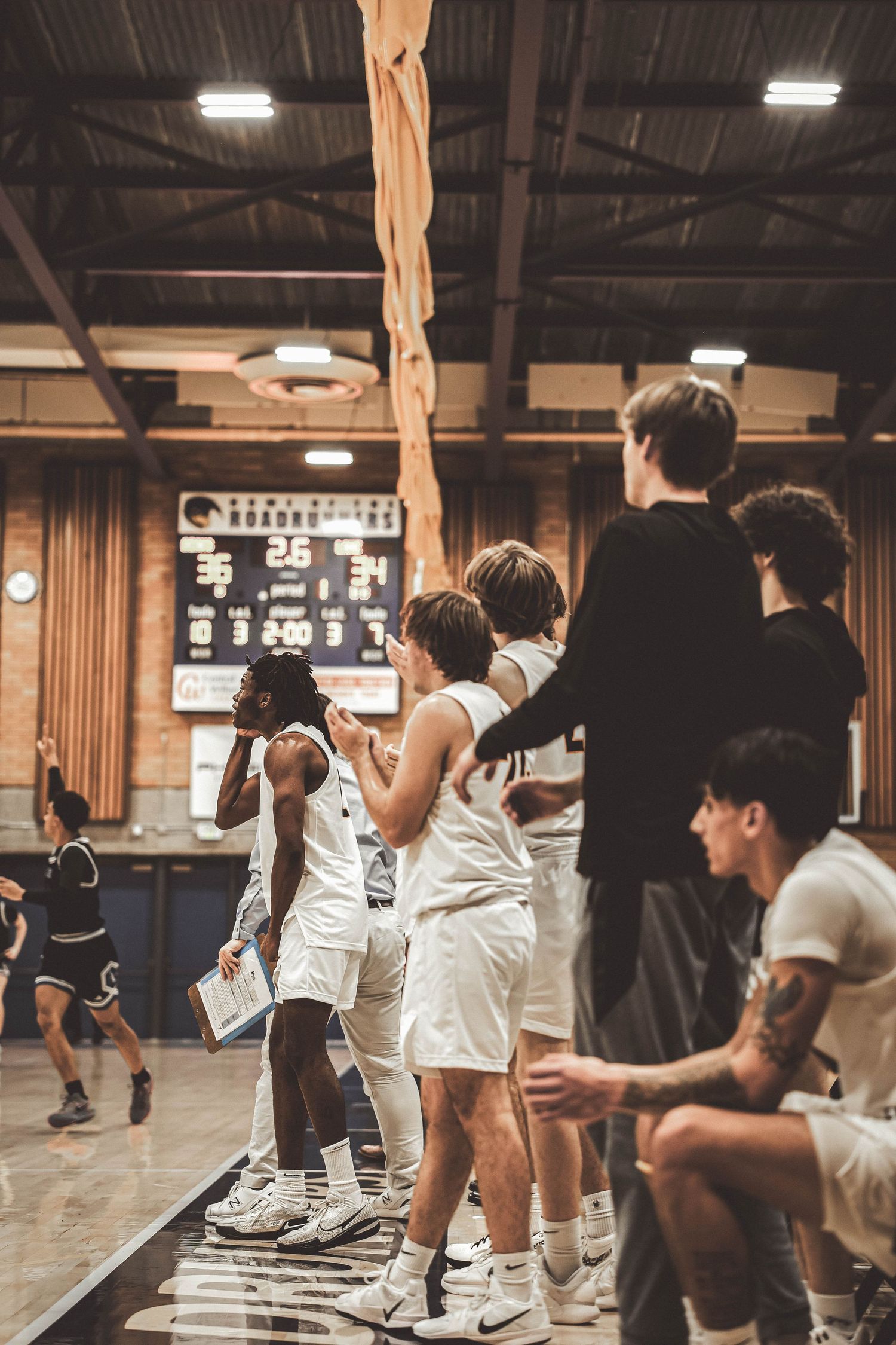 Basketball players in white uniforms warm up before a game in a wood-paneled gymnasium.