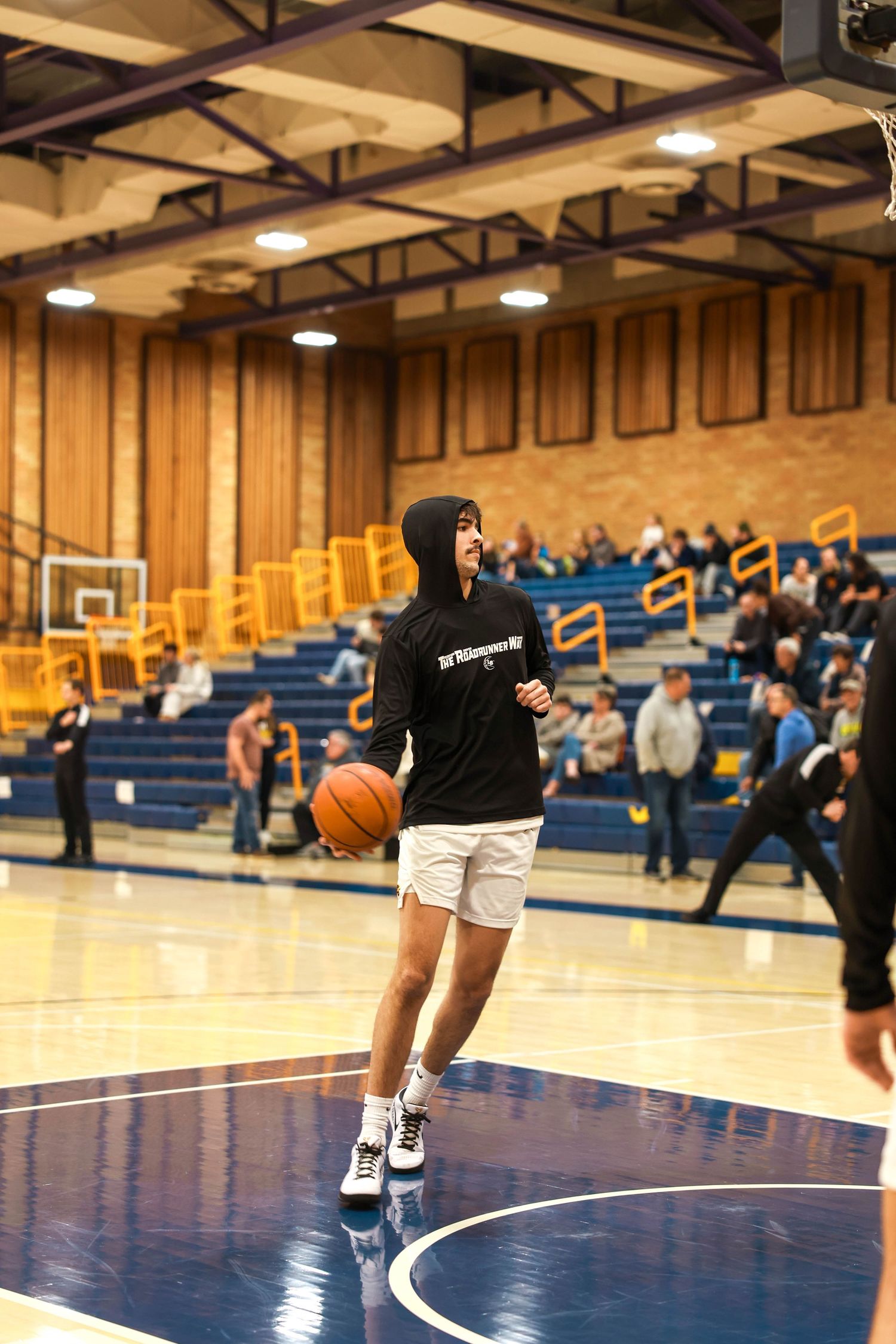 Empty basketball court with blue bleachers and wooden paneled walls in a school gymnasium.