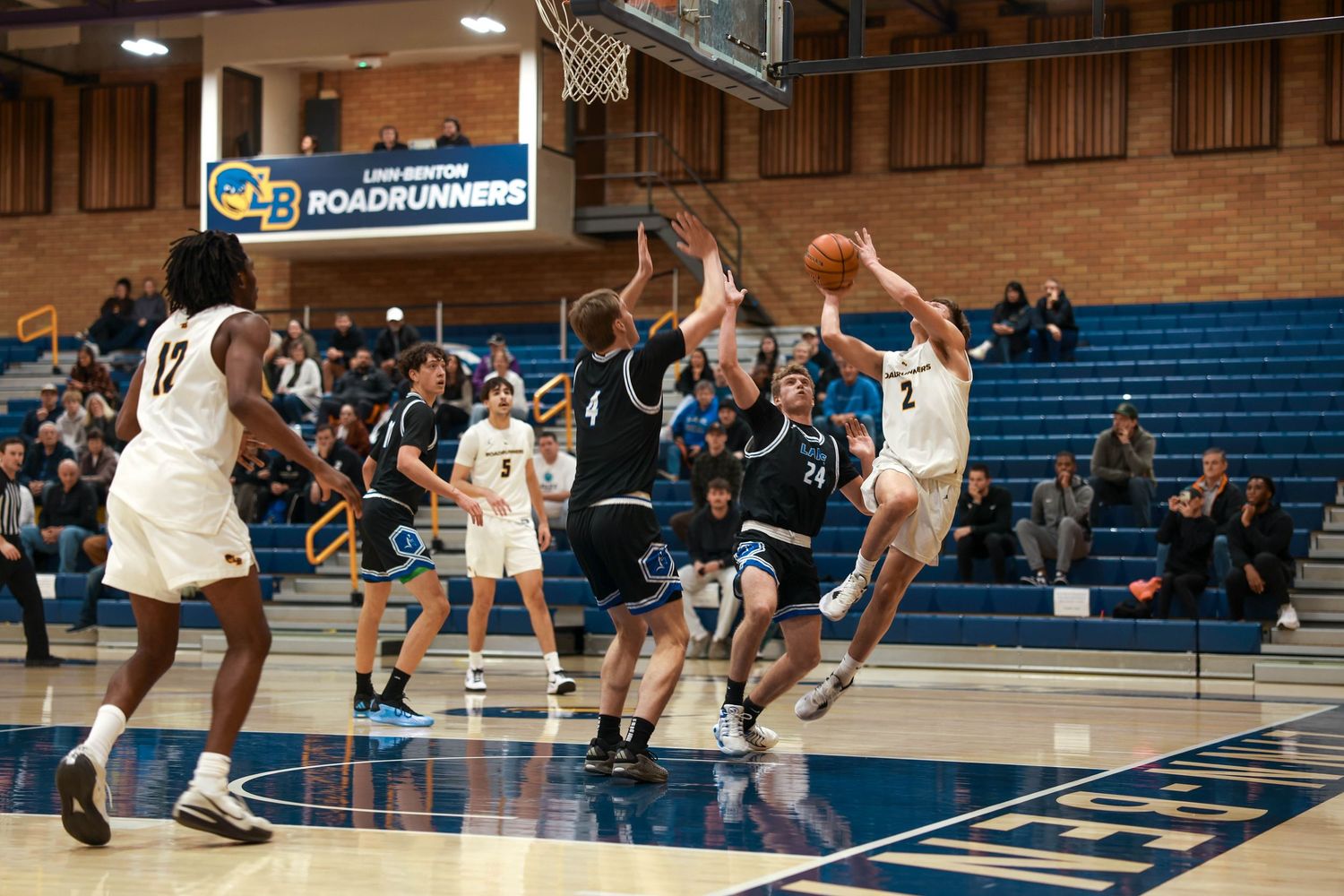 Basketball players in white and dark uniforms battle for position during a competitive match.