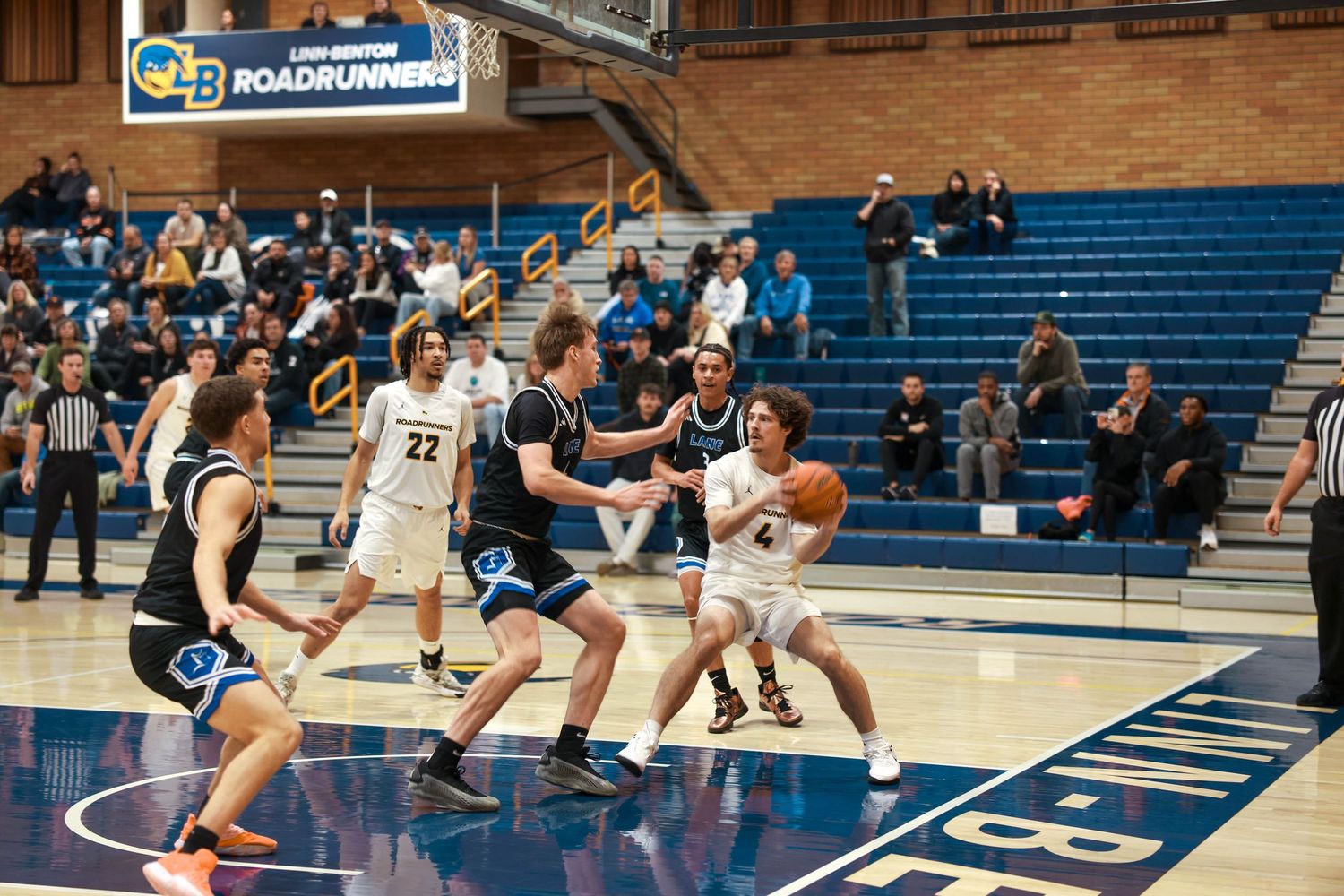 Basketball players in white and dark uniforms battle for position during a competitive indoor game.