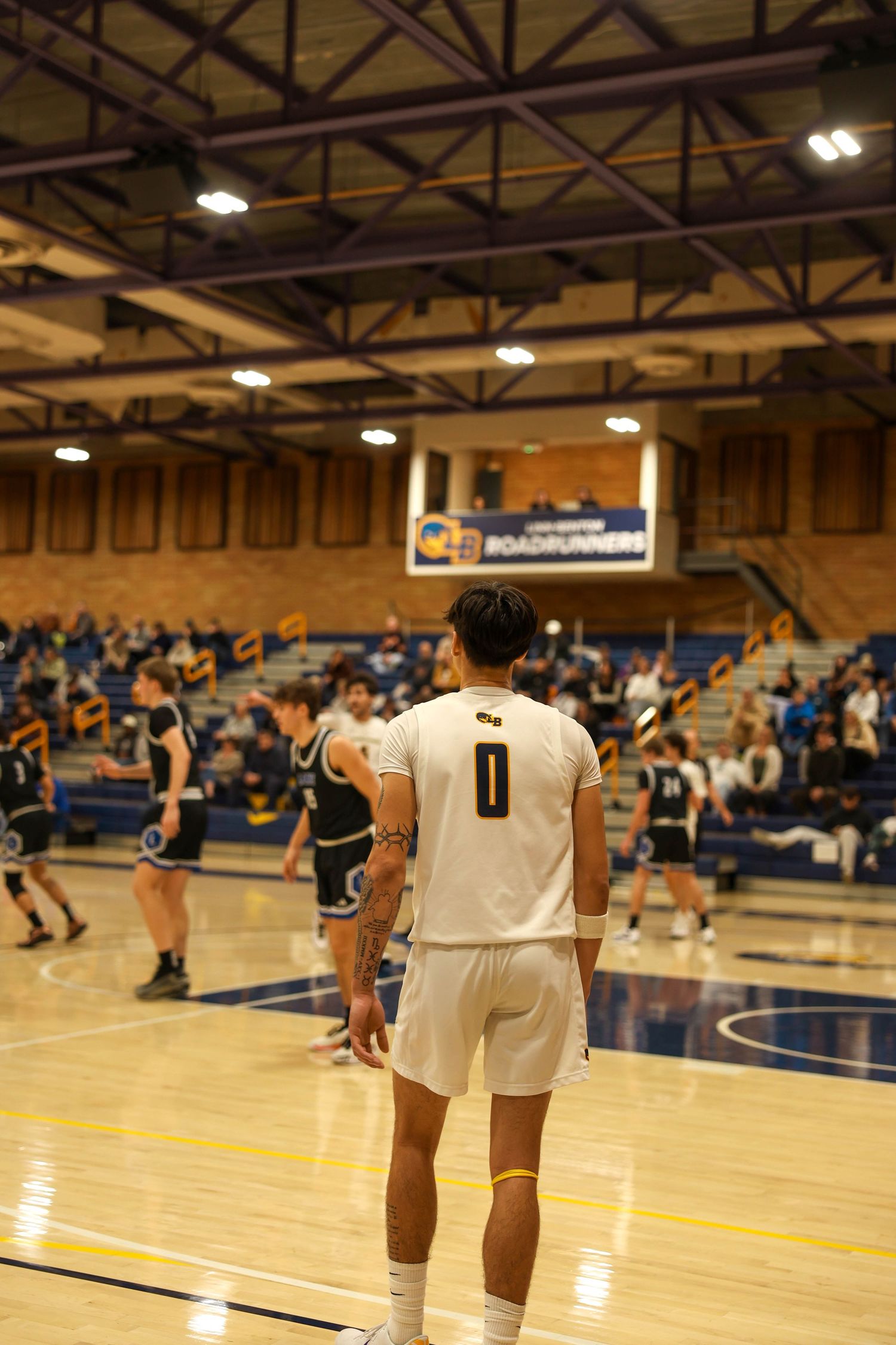 Wide shot of basketball court showing players spread out during gameplay with gym lighting overhead.