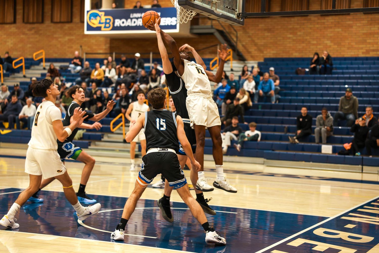 Players from opposing teams compete for position during an indoor basketball game.