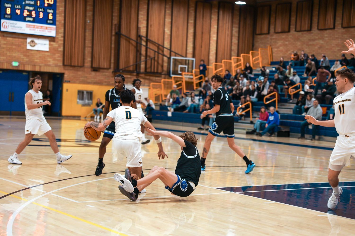 Basketball player falls to the court during an intense defensive play.