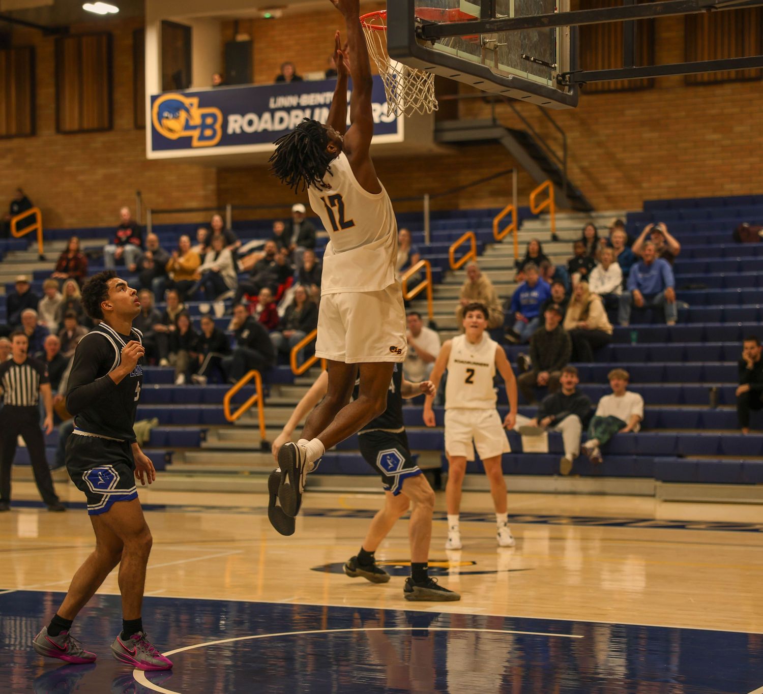 Basketball players compete in an intense game on a wooden court with blue bleachers in the background.