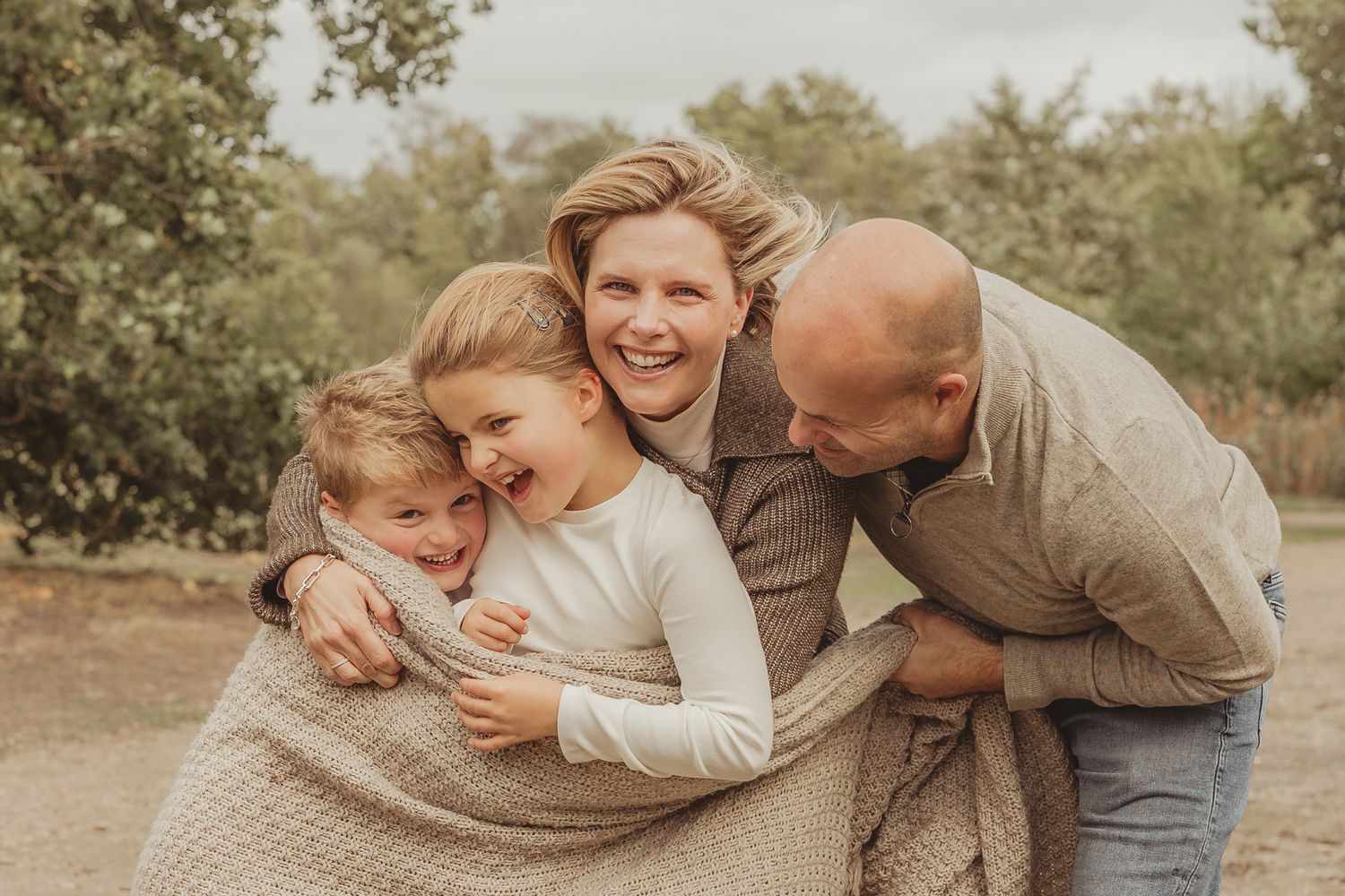 Joyful family embracing and laughing together outdoors in natural lighting.