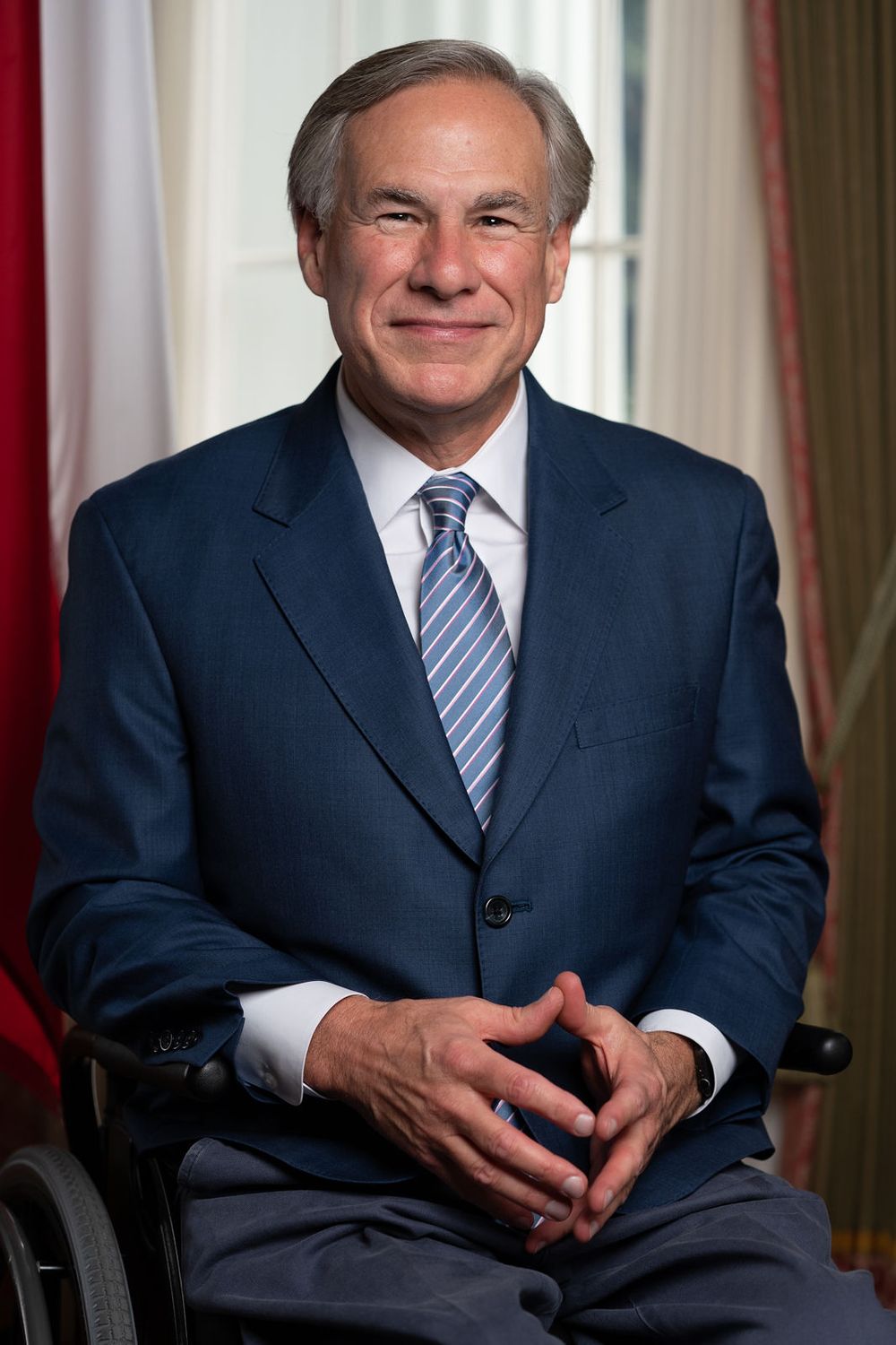Professional portrait of person in navy suit sitting in chair against red and white background.