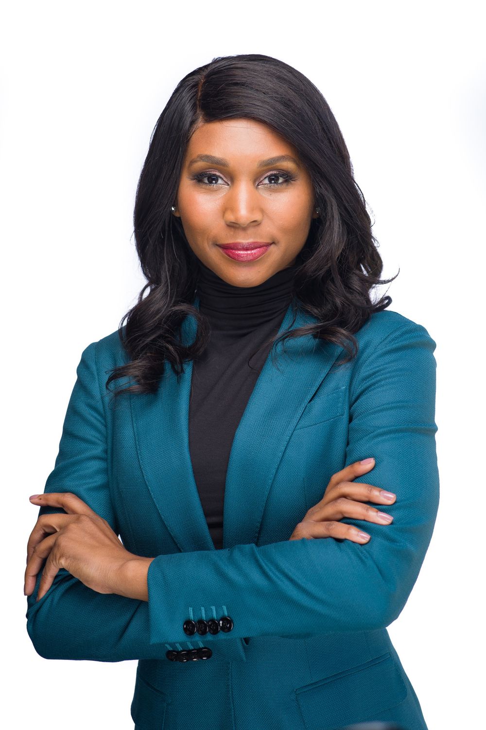 Professional wearing a teal blazer and black top poses with crossed arms against white background.
